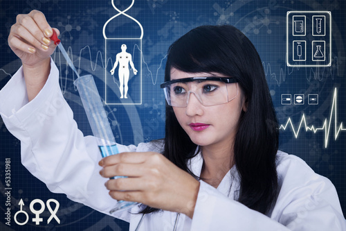 Photo: Attractive female scientist using pipette on blue background Attractive female scientist using pipette on blue background