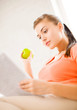 woman with green apple reading newspaper at home