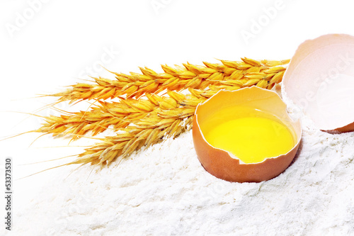 Photo: Spikelets of wheat with egg on flour spillage.Isolated. Spikelets of wheat with egg on flour spillage.Isolated.