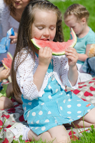 Photo: Pretty little girl eating watermelon in the park Pretty little girl eating watermelon in the park