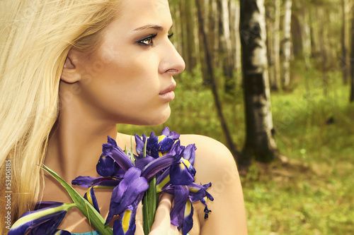 Photo: Beautiful blond woman with blue flowers in forest. summer Beautiful blond woman with blue flowers in forest. summer