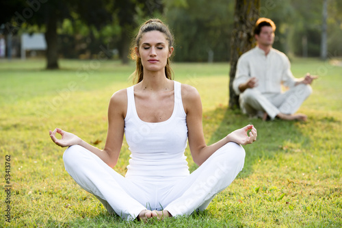 Photo: Young couple meditating in park Young couple meditating in park