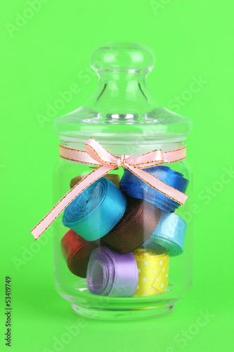 Photo: Glass jar containing various colored ribbons on green Glass jar containing various colored ribbons on green