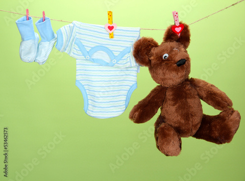 Photo: Baby clothes hanging on clothesline, on green background Baby clothes hanging on clothesline, on green background