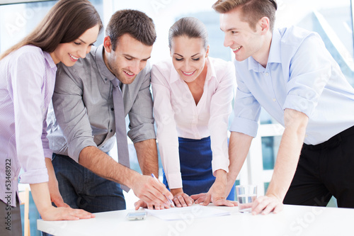 Photo: Coworkers leaning over table in office Coworkers leaning over table in office