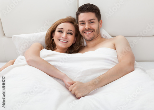 Photo: Portrait of happy young couple lying on bed Portrait of happy young couple lying on bed