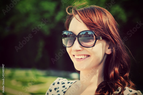 Photo: Young beautiful woman in sunglasses smiling in a summer park. Young beautiful woman in sunglasses smiling in a summer park.
