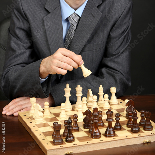 Photo: Young business man playing chess on black background Young business man playing chess on black background