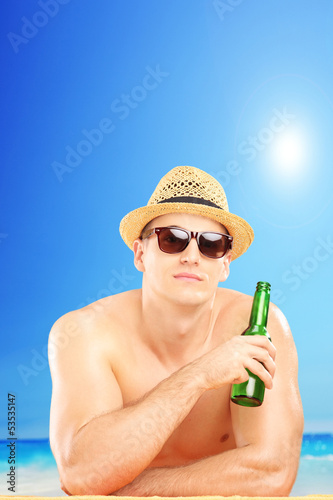 Photo: Smiling guy with hat and sunglasses drinking cold beer on a beac Smiling guy with hat and sunglasses drinking cold beer on a beac