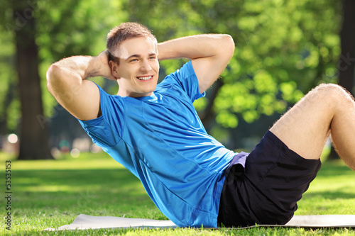 Photo: Young man athlete exercising abs in a park Young man athlete exercising abs in a park