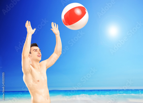 Photo: Young male playing with a beach ball, next to a sea Young male playing with a beach ball, next to a sea