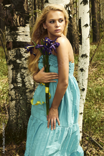 Photo: Beautiful blond woman with blue flowers walking in a forest Beautiful blond woman with blue flowers walking in a forest