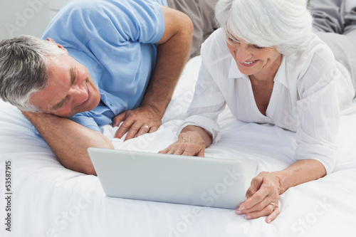 Photo: Cheerful couple using a laptop in bed Cheerful couple using a laptop in bed