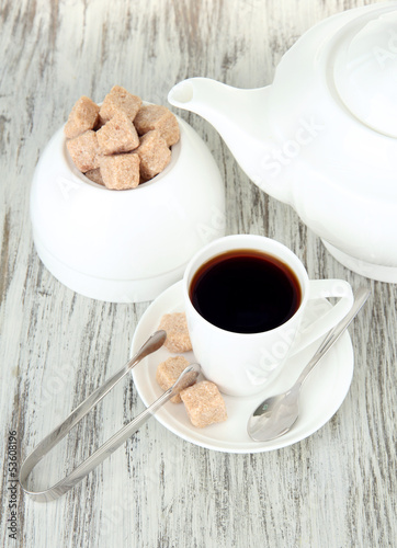 Photo: Cup of coffee, teapot and sugar-bowl on color wooden background Cup of coffee, teapot and sugar-bowl on color wooden background
