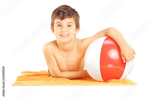 Photo: Smiling kid lying on a beach towel and holding a ball Smiling kid lying on a beach towel and holding a ball