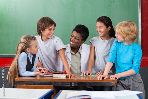 Photo: Happy Teacher With Students Communicating At Desk Happy Teacher With Students Communicating At Desk