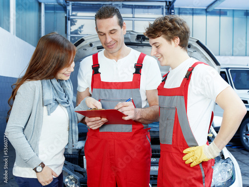 Photo: Customer and mechanics in a garage look at a quotation Customer and mechanics in a garage look at a quotation