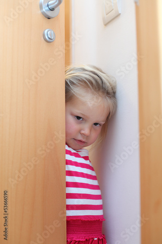 Photo: Shy little girl hiding behind the door Shy little girl hiding behind the door