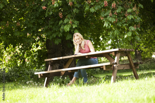 Photo: A young woman sitting on a garden bench reading a book, smiling A young woman sitting on a garden bench reading a book, smiling