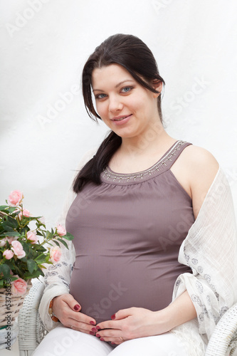 Photo: Happy pregnant woman sits in the room with flowers Happy pregnant woman sits in the room with flowers