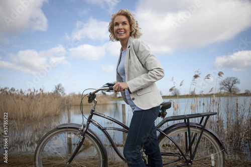 Photo: A mid adult woman pushing a bicycle next to a lake A mid adult woman pushing a bicycle next to a lake