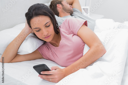 Photo: Woman texting while her partner is sleeping Woman texting while her partner is sleeping
