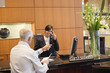 Photo: Receptionist talking on a landline phone with a businessman pointing at the hotel reception counter Receptionist talking on a landline phone with a businessman pointing at the hotel reception counter