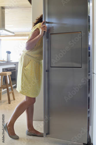 Photo: Woman looking into a refrigerator in the kitchen Woman looking into a refrigerator in the kitchen