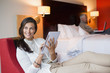 Photo: Woman using a digital tablet in a hotel room with her husband using laptop in the background Woman using a digital tablet in a hotel room with her husband using laptop in the background