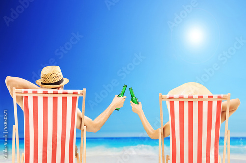 Photo: Man and woman relaxing on a beach and cheering with beers Man and woman relaxing on a beach and cheering with beers