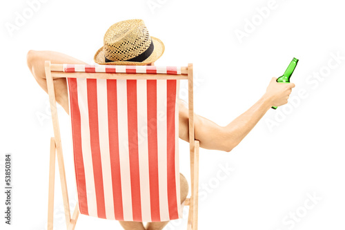 Photo: Man with hat sitting on a beach chair and holding a beer bottle Man with hat sitting on a beach chair and holding a beer bottle