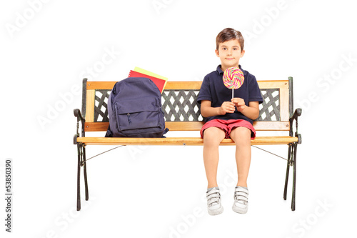 Photo: School boy sitting on a bench and holding a candy lollipop School boy sitting on a bench and holding a candy lollipop