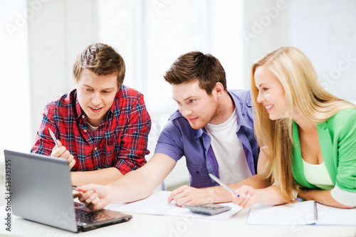 Photo: smiling students looking at laptop at school smiling students looking at laptop at school