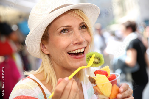 Photo: Cheerful blond girl eating fresh fruits in summer Cheerful blond girl eating fresh fruits in summer