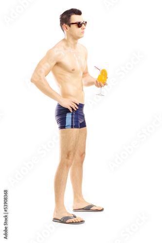Photo: Full length portrait of a guy in swimming shorts holding a cockt Full length portrait of a guy in swimming shorts holding a cockt