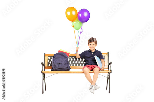 Photo: Schoolboy sitting on a wooden bench with books and holding a bun Schoolboy sitting on a wooden bench with books and holding a bun