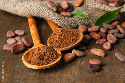 Photo: Cocoa powder in spoons and cocoa beans on wooden background Cocoa powder in spoons and cocoa beans on wooden background