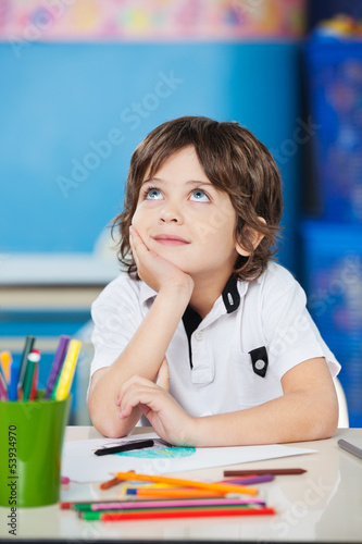 Photo: Boy Looking Up While Sitting With Hand On Chin At Desk Boy Looking Up While Sitting With Hand On Chin At Desk