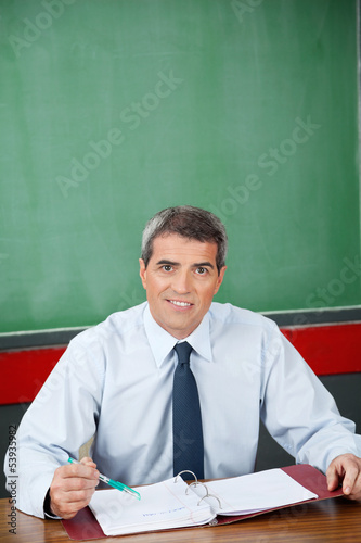Photo: Professor With Binder And Pen Sitting At Desk Professor With Binder And Pen Sitting At Desk