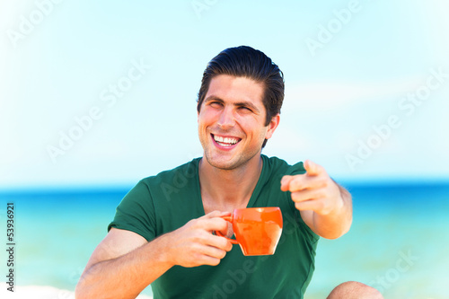 Photo: Handsome young man with cup at beach background Handsome young man with cup at beach background