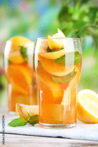 Photo: Iced tea with lemon and mint on wooden table, outdoors Iced tea with lemon and mint on wooden table, outdoors