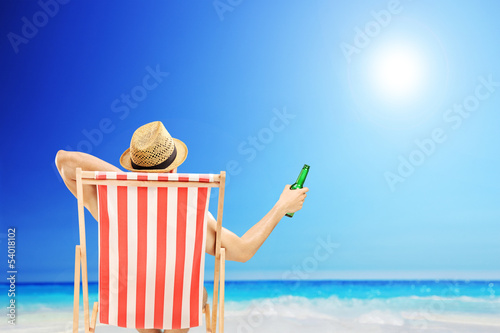 Photo: Man with hat sitting on a beach chair and holding a beer Man with hat sitting on a beach chair and holding a beer