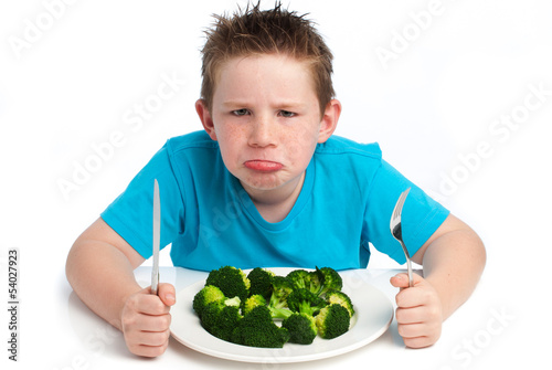 Photo: Grumpy young boy not happy about eating broccoli. Grumpy young boy not happy about eating broccoli.