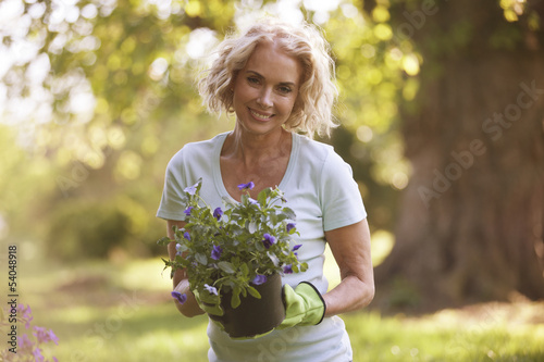 Photo: A mature woman holding a plant pot containing pansies A mature woman holding a plant pot containing pansies