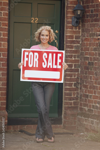 Photo: A mature woman holding a property for sale sign A mature woman holding a property for sale sign