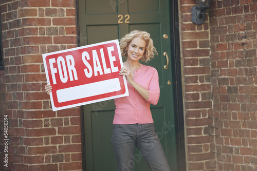 Photo: A mature woman holding a property for sale sign A mature woman holding a property for sale sign