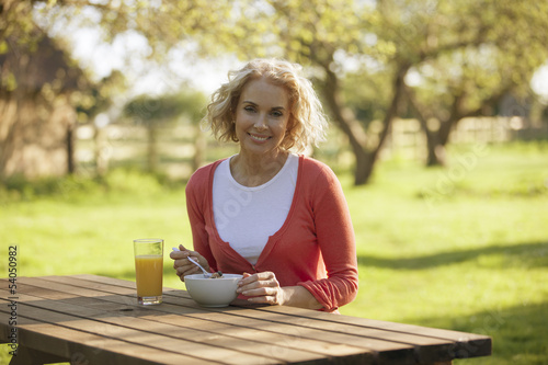 Photo: A mature woman sitting at a garden bench eating breakfast A mature woman sitting at a garden bench eating breakfast