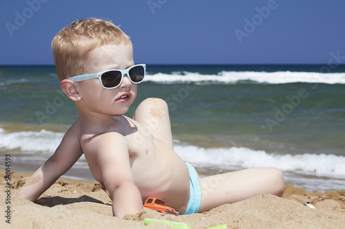 Photo: child sitting on the beach in sand. little boy near the sea child sitting on the beach in sand. little boy near the sea