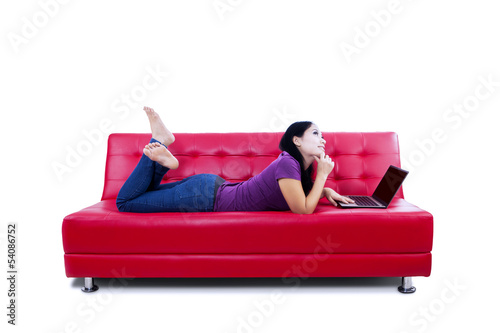 Photo: Thoughtful woman with laptop on couch Thoughtful woman with laptop on couch