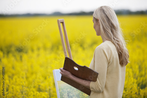 Photo: A young woman painting a picture of a rape seed field in flower A young woman painting a picture of a rape seed field in flower